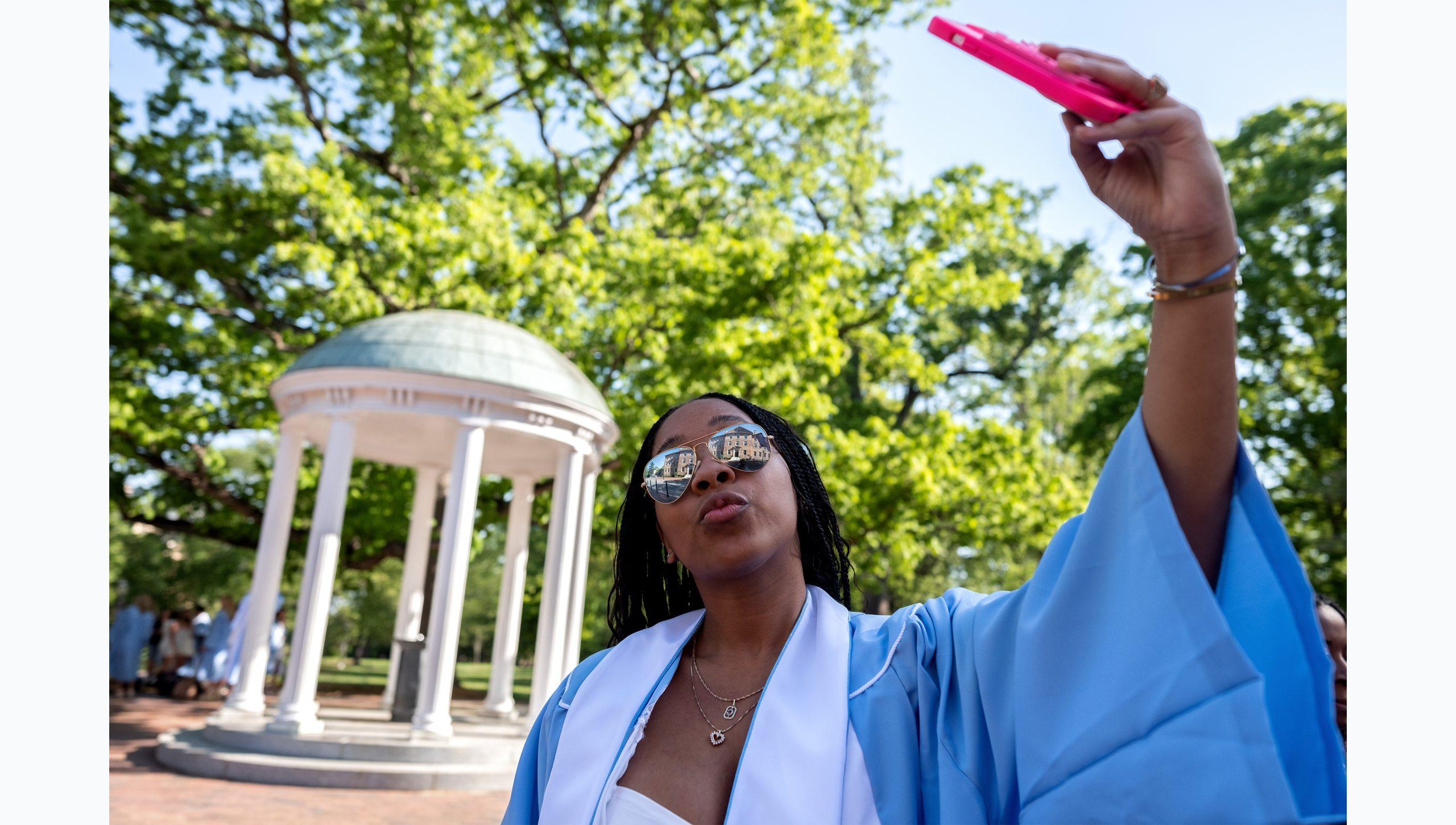 A student taking a selfie in her regalia near the Old Well.